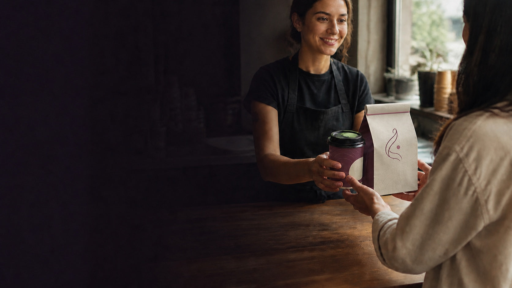 Coffee shop team member presenting a premium patterned package and takeaway drink to a customer